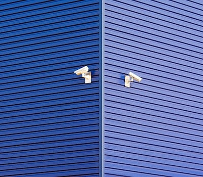 Installation vidéosurveillance | Videoconsult, expert en installation de caméra de surveillance en copropriété. Image représentant deux caméras de surveillance accrochées sur un mur peint en bleu. @pexels-jan-van-der-wolf-10932824